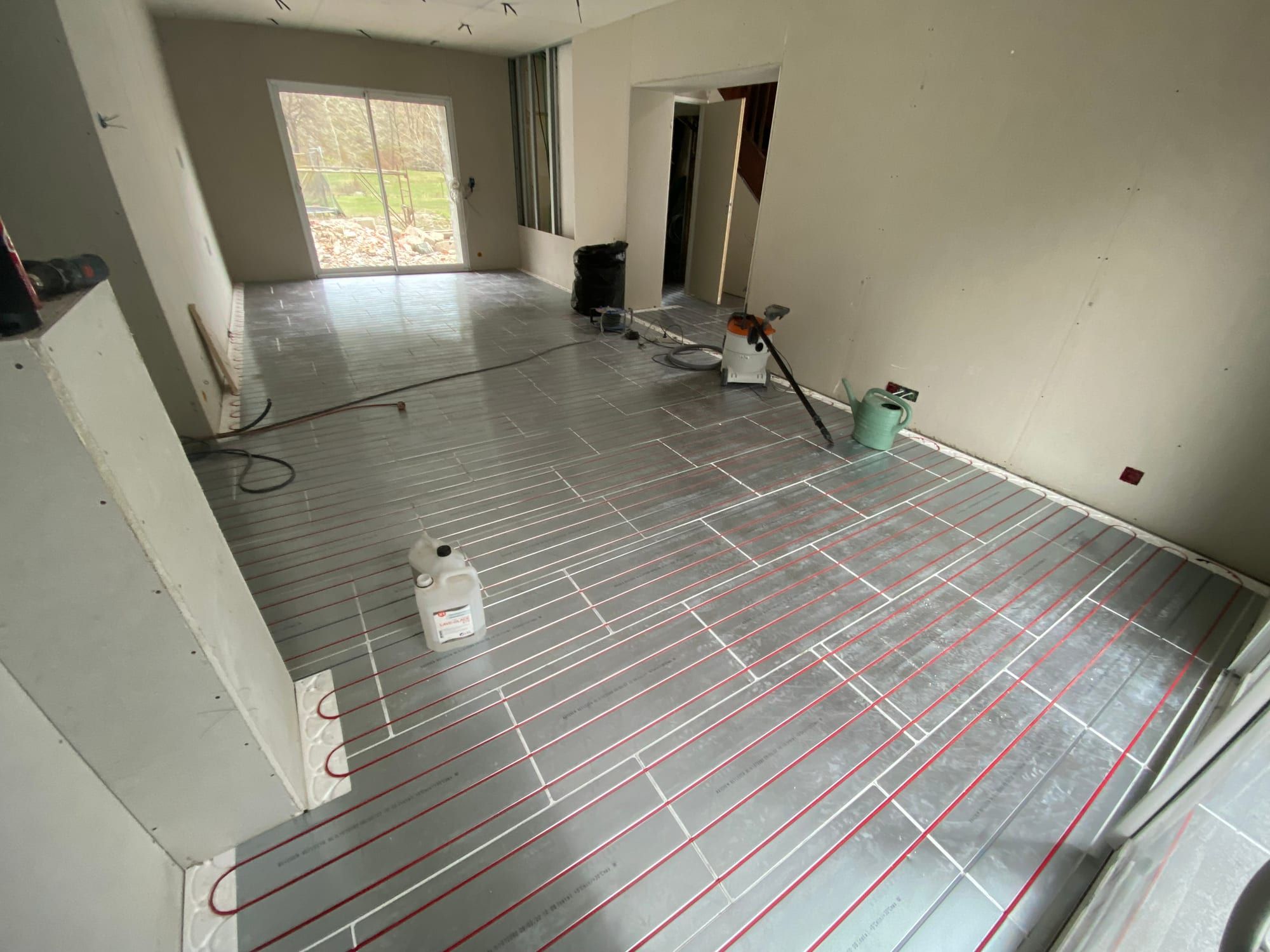 Tubes rouges de plancher chauffant posés sur des plaques à plots, grande pièce en travaux